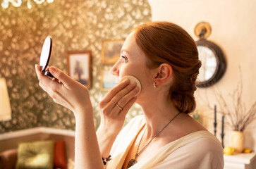 young girl powdering her face in front of a mirror