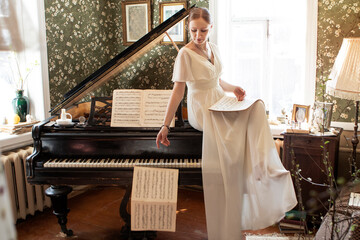 a girl in a long white dress sits on a piano and holds notes in her hands