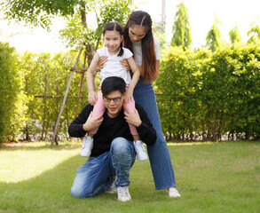 Asian family happy bright cute daughter is resting by playing in the grass let daughter ride father's neck