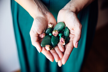 A woman holds in her hands several malachite stones with several dry pink roses. She is wearing a pretty emerald green dress.. - obrazy, fototapety, plakaty