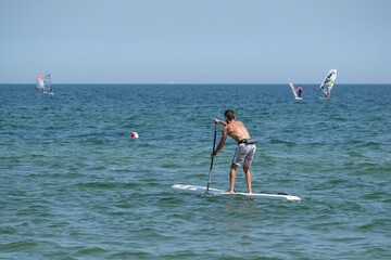 The man is swimming with the stand up paddle on the sea.