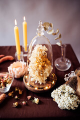 Beautiful still life with an urn filled with dried flowers, a bowl filled with small dried roses, several lighted candles, and a lotus-shaped candlestick..
