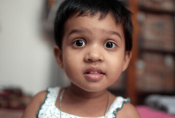 Monochromatic portrait of a little Bengali (Indian ethnicity) girl with expressive face, looking at camera. Photo taken inside her room.