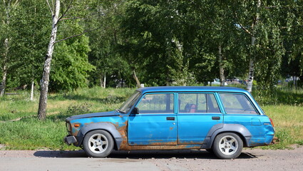 An old blue rusty Soviet car is parked on the street, Badaeva Street, St. Petersburg, Russia, July 2022
