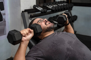 A man in his late 30s makes a comeback at the gym. Doing incline dumbbell bench presses with a...