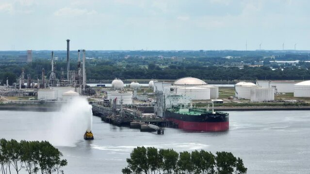 Oil tanker ship docking in the port of Rotterdam in The Netherlands seen from above with oil storage silos in the bakcground. Drone view