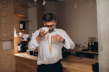 Man is spilling coffee on white shirt while drinking in office..
