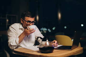 Caucasian boss working late sitting on desk in office at night. Business man feeling tired and stress for overload job..