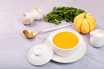 Flat lay of Pumpkin Cream soup served with seeds on gray concrete background. Top view of Autumn cream-soup in country style and fallen autumn maple leaves. Useful dietary snack and lunch