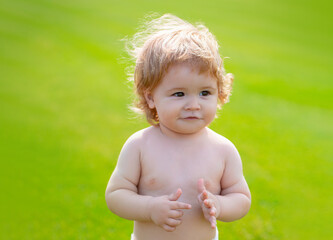 Happy baby in grass on the fieald at sunny summer evening. Smiling child outdoors. Funny little child closeup portrait. Kids emotion, happy smiling face.