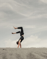 Fototapeta premium Young man stands on hands on the sand in desert