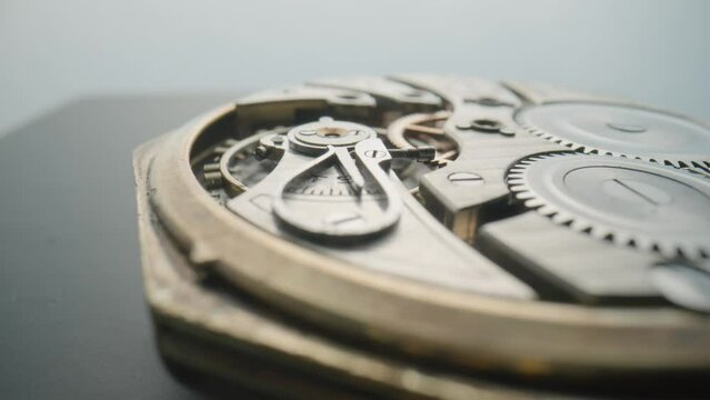 An antique pocket watch with open working clock mechanism rotates on gray studio background. Reverse side of clock with rotating gears, spring and gearwheel. Disassembled retro pocket watch close up.