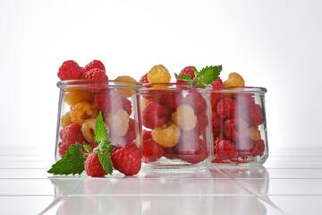 Raw organic yellow and red sunshine raspberries in a glass jar on a white background. Focus on center