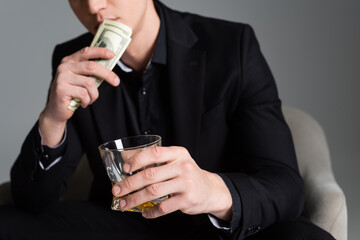 cropped view of blurred man with dollars and glass of whiskey isolated on grey.