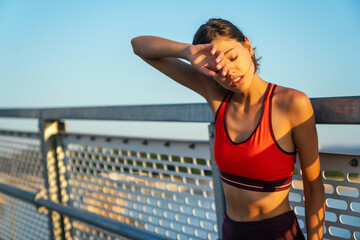 Portrait of tired fitness young woman takeing a break during workout in the city.