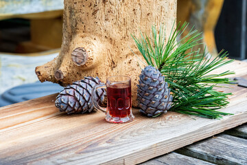 a glass swiss stone pine schnapps, cones and twigs from the swiss stone pine or arolla on a wood board - obrazy, fototapety, plakaty