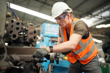 Young Caucasian hardworking heavy industry worker in protective suit and helmet using tablet and screwing valve.