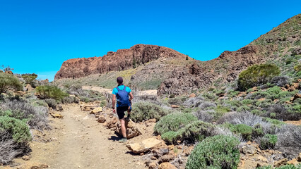Fototapeta na wymiar Man with backpack hiking to Riscos de la Fortaleza near Pico del Teide, Mount El Teide National Park, Tenerife, Canary Islands, Spain, Europe. Path via La Canada de los Guancheros dry desert plain