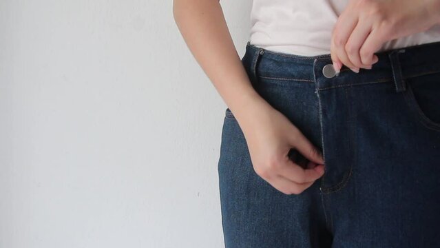 Closeup of female getting dressed wearing jeans  standing on gray background.