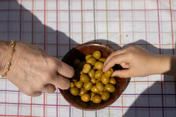 A child and an adult hand picking up seasoned green olives, typical Spanish snack, always eaten in...