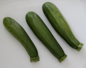 Three assorted green courgettes lying on a plain white background