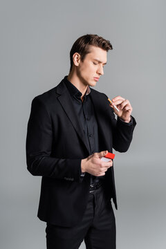 man in black suit holding cigarette and pack isolated on grey.