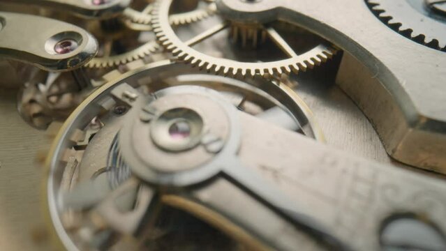 Moving metal gears inside working pocket watch mechanism. Working clock mechanism with rotating spring, gears, gearing and toothed wheels. Inside view of a moving clockwork. Macro shot. Rack focus.