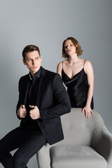 passionate woman in strap dress near man in formal wear looking away isolated on grey.