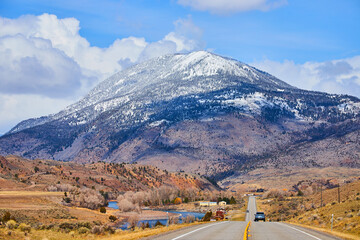 Two-lane paved road in mountains leading towards huge snowy mountain in western America