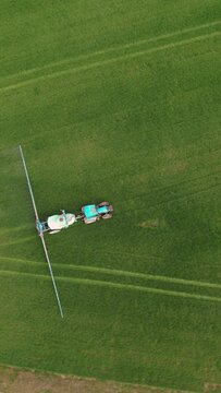 AERIAL, TOP DOWN: Blue tractor with modern farm equipment fertilizing crop field. Working farmer maintaining cultivated farm field with modern farming equipment. View of a tractor watering a field.