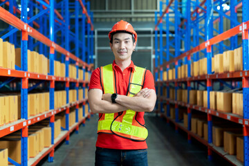 Handsome Smiling Worker Wearing Hard Hat, Standing with Crossed Arms in the Retail Warehouse full of Shelves with Cardboard Boxes. Professional Working in Logistics, Delivery, and Distribution Center