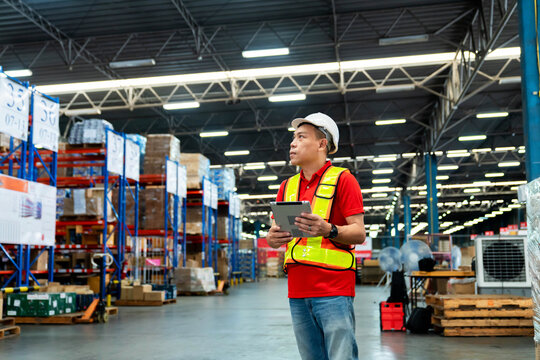 Warehouse Worker in safety suite working with tablet computer to record data the stock inventory in large warehouses, a Smart warehouse management system.