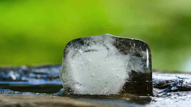 Ice cube is melting on a stone., time lapse on green