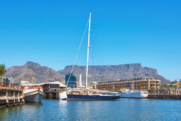 Fototapeta na wymiar Sailboats docked at a harbor with Table Mountain in the background against blue sky with copy space. Scenic landscape of waterfront port at a marina dockyard. Nautical vessels for travel and tourism