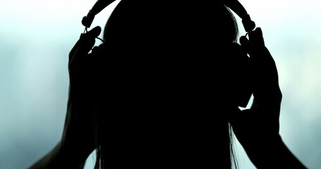 Back of woman putting headphones on, silhouette of person listening to music, song, podcast, or audiobook