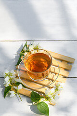 Jasmine tea in glass cup and flowers on a wooden white background, natural light photo with hard shadows. Cup with green jasmin tea