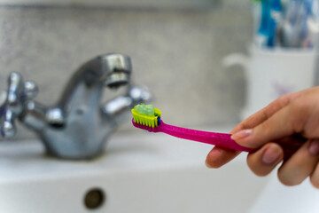A girl is brushing her teeth and teeth braces with a special brush during the day in her bathroom