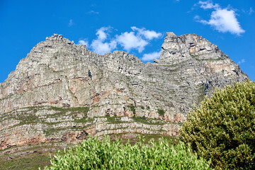 Below view of majestic mountains with bushes growing below and cloudy blue sky copy space above. Nature landscape of mountain rock outcrops with wild green plants during a bright and beautiful day