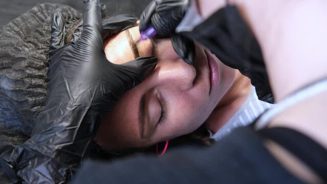 Eyebrow tattoo artist doing procedure to female client. Close-up view