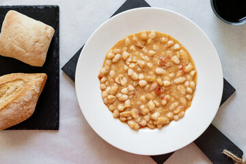 Top view, beans cooked with vegetables, on a white plate, accompanied by rustic bread.