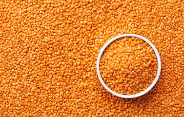 ceramic plate with raw red lentils on a red lentils background close-up top view.