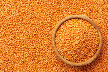wooden plate with raw red lentils on a red lentils background close-up top view.