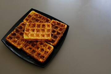 Sweet waffles prepared for serving. A tasty dessert eaten with fruit and preserves. Dark background.