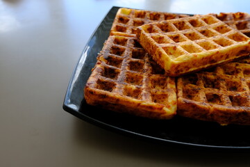 Sweet waffles prepared for serving. A tasty dessert eaten with fruit and preserves. Dark background.