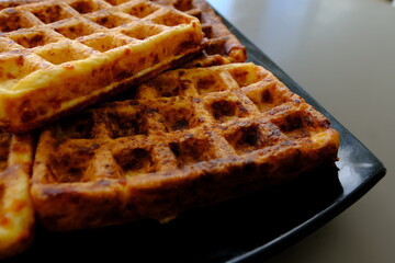 Sweet waffles prepared for serving. A tasty dessert eaten with fruit and preserves. Dark background.