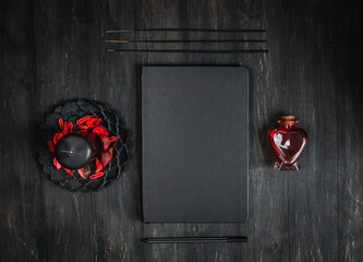 Black leather book, candle, red potion, ritual sticks and pen on a black background.