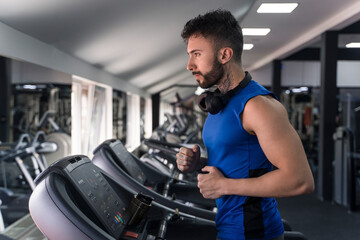 Fototapeta na wymiar Handsome male with tattoos in his 20s running on the treadmill in the gym