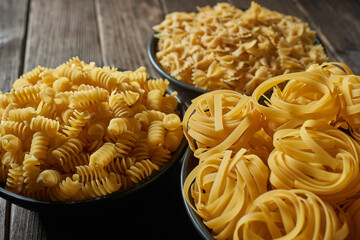 Three deep bowls with uncooked pasta on a wooden table. Assortment of raw macaroni