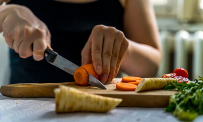 Obraz na płótnie Canvas A girl is cutting carrot and vegetables on a wooden cutting board during the day