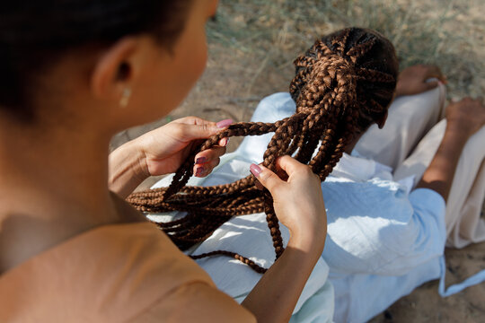 A woman holds her friend's braids in the hands 
